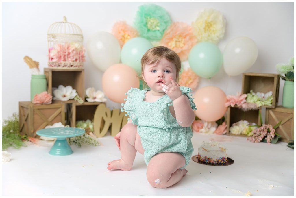 first birthday baby girl with frosting and peach and mint decorations