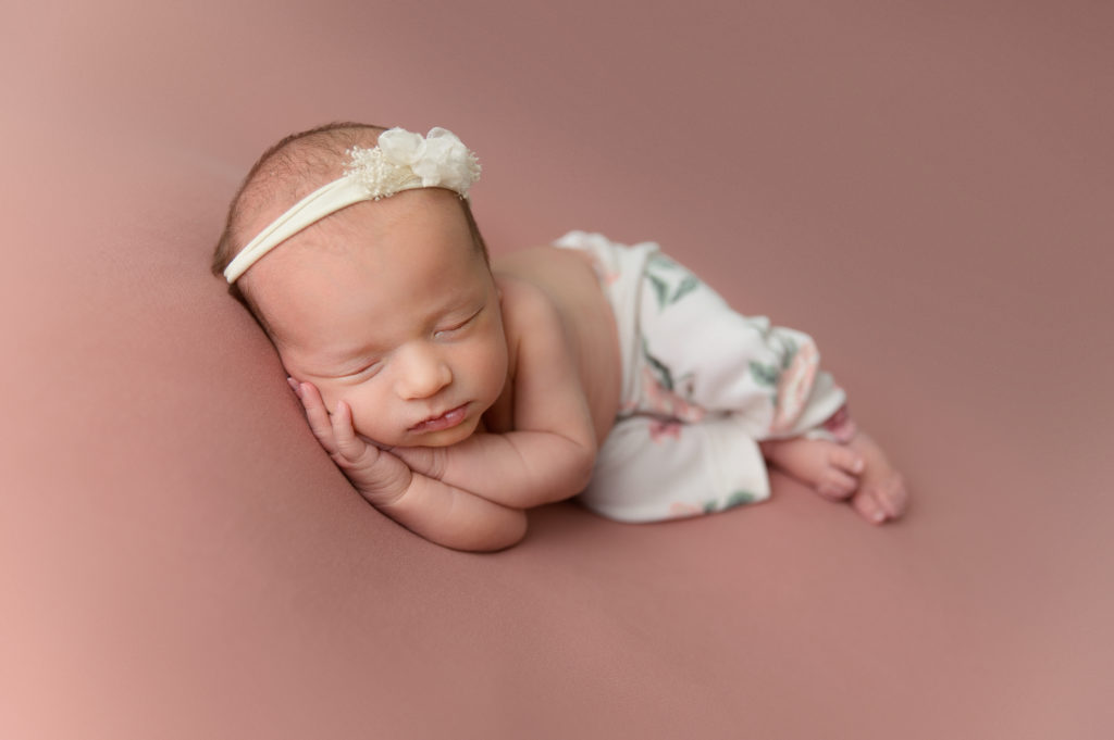 newborn baby girl side lying pose on pink fabric