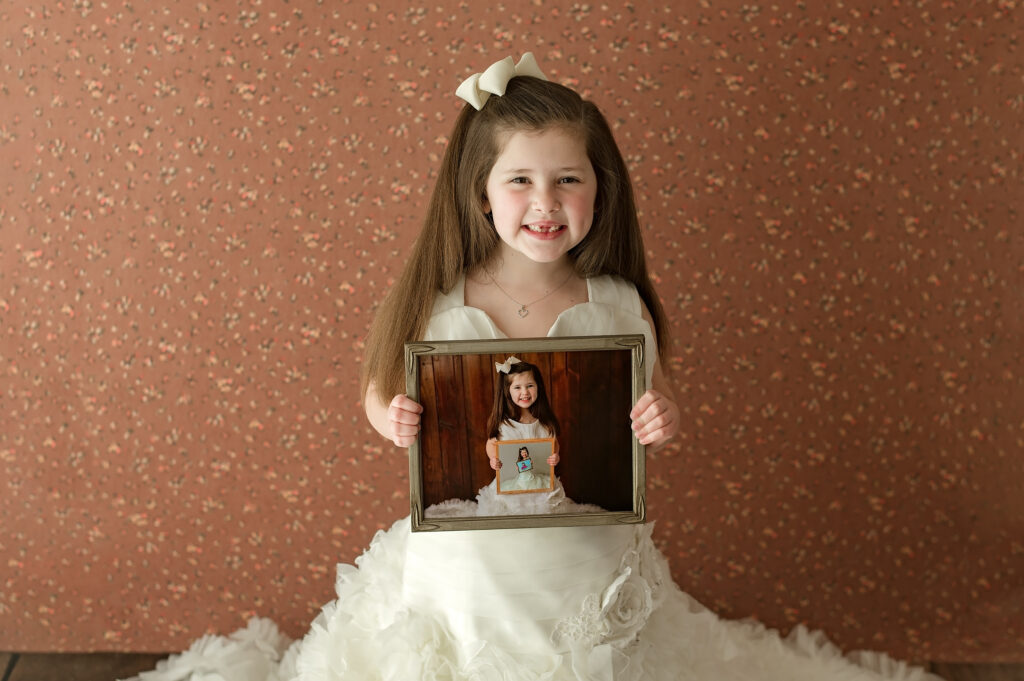 little girl wearing her moms wedding dress holding picture of her from previous years in the same dress