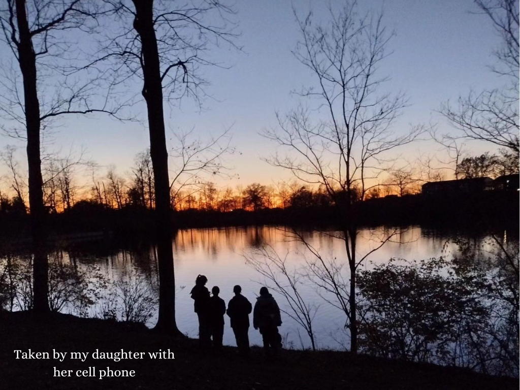 silhouette of four girls standing by a lake at sunset 